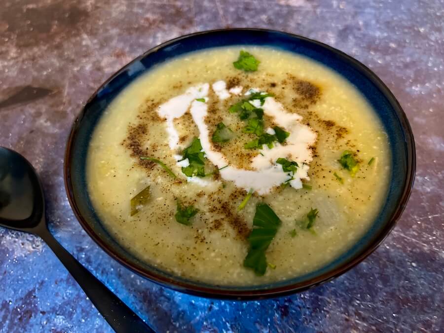 Dark blue bowl filled with creamy vegan leek and potato soup with black pepper, fresh parsley and a swirl of vegan cream on top