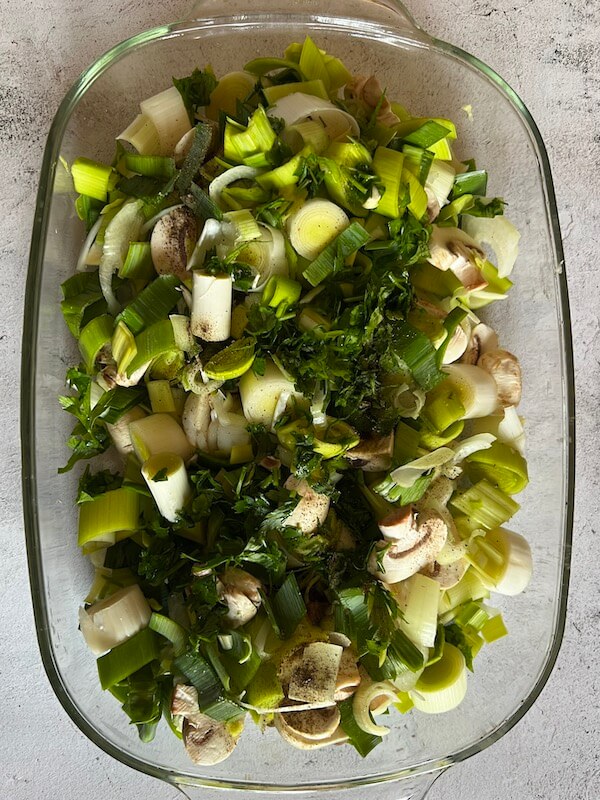 Leeks and mushrooms with fresh parsley in the base of a casserole dish, ready for the addition of the potato slices.
