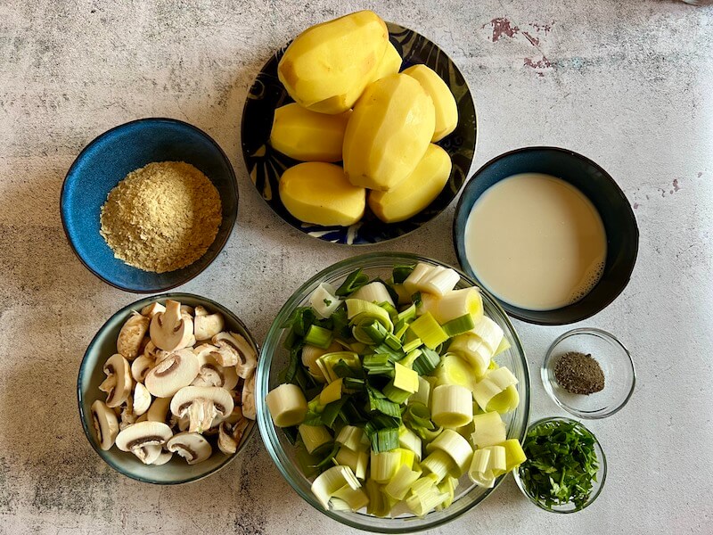 Ingredients for vegan leek & potato bake - potatoes, plant milk, leeks, mushrooms, nutritional yeast, ground black pepper and fresh parsley