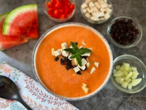 Bowl of watermelon Gazpacho with toppings of watermelon, red pepper, tofu, raisins and cucumber