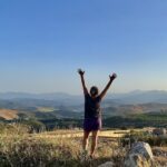 What is mindset coaching? Woman reaching for the sky with far reaching views of the mountains in the background
