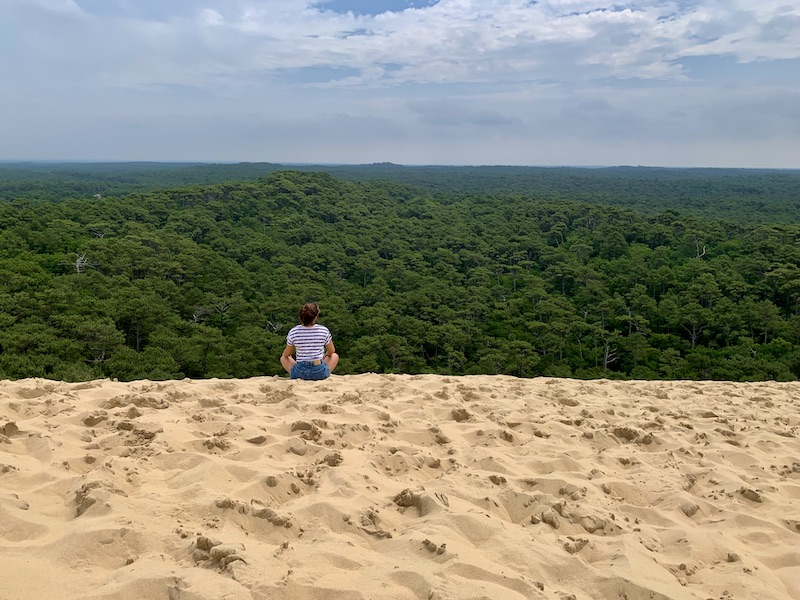 Why do I feel like a failure? Girl sitting crosslegged on the sandy horizon overlooking a forest