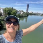 Stop seeking external validation - smiling woman with arms thrown upward, standing in front of the Guadalquivir River in Seville