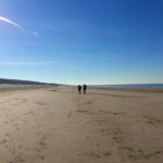 Strengthen your relationship - couple walking on a sandy beach with blue skies above